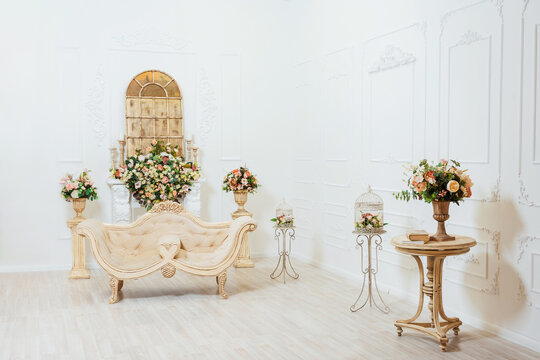 light sofa with a fireplace and a golden mirror. bright classic room with a beige sofa and artificial flowers. photo zone for wedding photo shoots in a photo studio