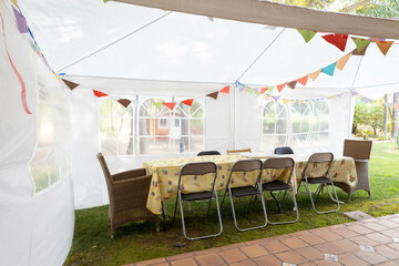 Tent ready for a birthday party with the family, with some colourful flags, and a table with some  different chairs
