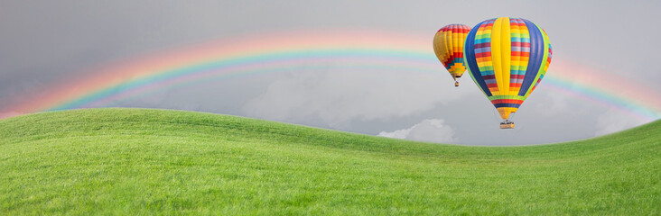 Hot Air Baloons Drift Above Grass Field with Rainbow in the Sky.