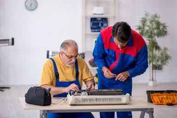 Two male repairmen repairing air-conditioner