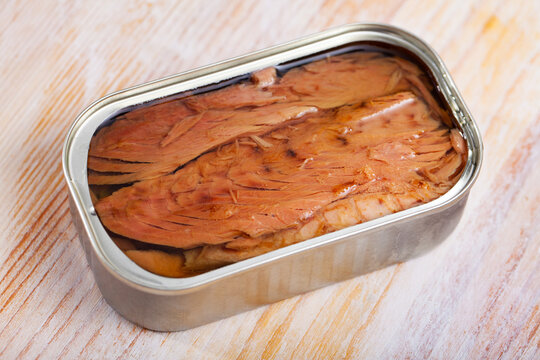 Open can of preserved natural fillet of frigate tuna on wooden table..
