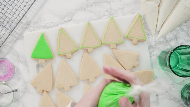 Flat lay. Stp by step. Icing Christmas tree-shaped sugar cookies with green royal icing.