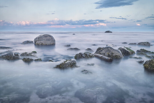 Purple sunset on the ocean, long exposure of rocks in the water