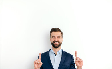 Positive attractive caucasian man, in elegant suit, pointing up with fingers hands gesture at empty space for presentation or advertising, stand on isolated white background, looks up, smiles