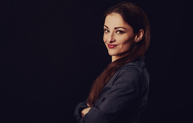 Beautiful thinking toothy smiling business woman with folded arms in blue shirt on black background with empty copy space for text. Closeup