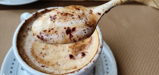 Aromatic coffee with foam and chocolate. Delicious cappuccino in a cup. Nice foamy coffee. Coffee foam on a spoon.