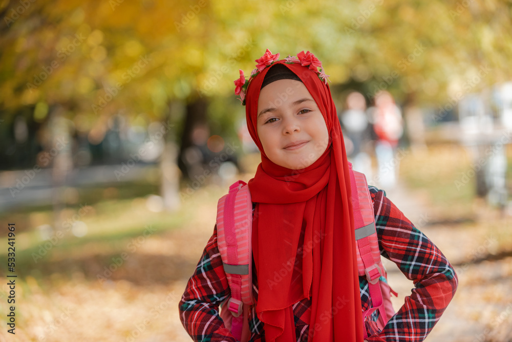 Wall mural a portrait of a happy muslim student girl in fashion hijab with school backpack in the the autumn pa