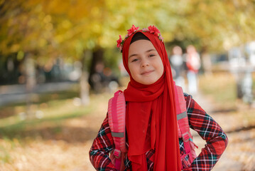 A portrait of a happy Muslim student girl in fashion hijab with school backpack in the the autumn park.	