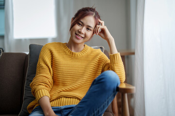 A portrait of a young Asian woman resting with a smiling face on the sofa by the window of the house