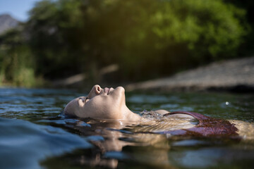 Beautiful latin young woman bathes in a lake. Smiling woman lying on her back floating in the sea water, relaxing on a beautiful summer day