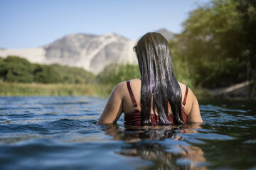 Fototapeta premium Beautiful young latin woman bathes in a lake enjoying a summer day. It stands at the bottom of the shoulders in the water.