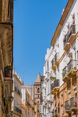 Fototapeta na wymiar Colorful street with balconies and tower of San Lorenzo Parish church in the background, Cádiz SPAIN