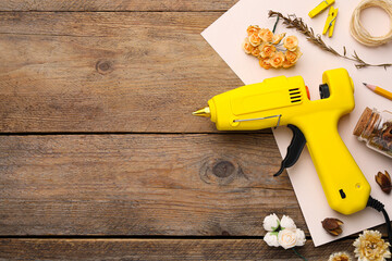 Hot glue gun and handicraft materials on wooden table, flat lay. Space for text