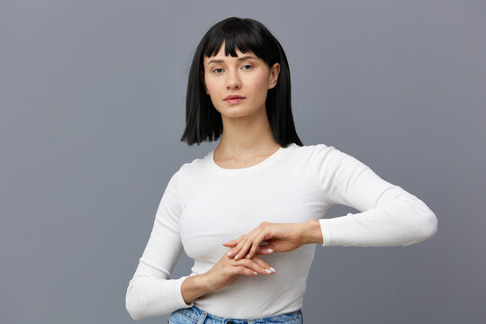 a calm, relaxed woman stands against a dark background in a tight white T-shirt, looks away, hands folded in front of her