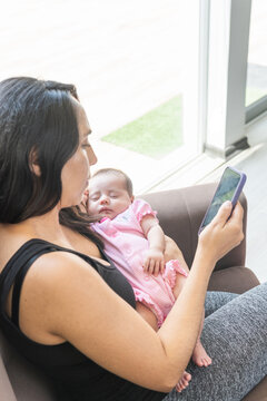 vertical photo of a mother working on her cell phone with her baby in her arms