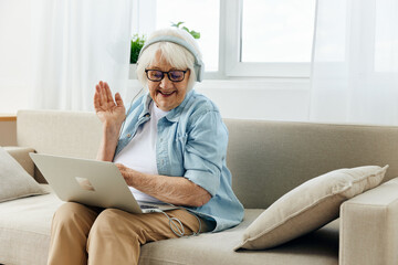 an elderly lady leads a remote lecture by video link teaching young people holding a laptop on her lap listening through headphones and sitting relaxed on the couch