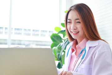 Asian female doctor sitting in office use a laptop computer Online video call talks to patients...