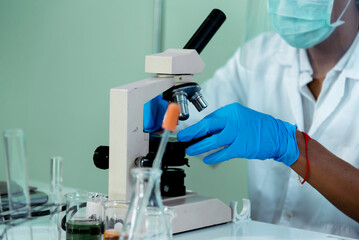 Fototapeta premium Close up African american Scientist man hands look into Microscope research in science laboratory. Crop biochemistry scientist hands using microscope in laboratory chemistry labs medical researcher