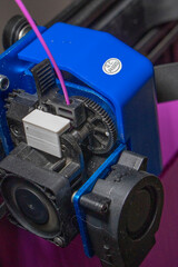 extrusor de una impresora 3d con filamento de color purpura o morado. Se ven los engranajes