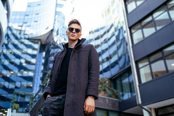 Handsome young man with sunglasses in coat in urban environment 