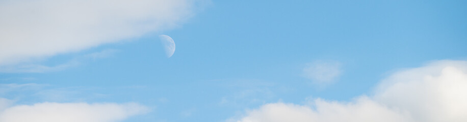 Peaceful blue sky with white clouds and a half moon, as a nature background
