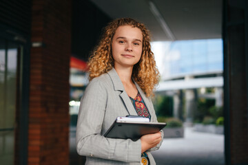 Fototapeta na wymiar Portrait of a woman college student happily looking at camera holding laptop outdoors after school on campus. Happy teenager portrait. Smart looking girl