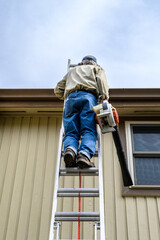 Closeup of a senior man climbing a ladder with a leaf blower, fall maintenance
