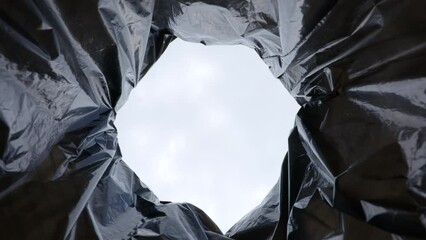 Low angle responsible male dropping plastic bottle into garbage recycling waste bag