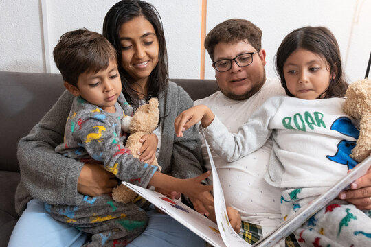 Pareja latina leyendo con sus dos hijos en el sillon 