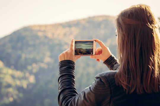 a woman takes photos of the forest and nature in the mountains on her phone, a view from the back. travel and landscapes in autumn, spring and summer, outdoor activities