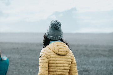 Woman on the black sand beach in Iceland, winter clothes.Shot from behind.Travel to iceland concept.