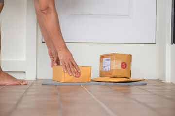 Woman collects parcel at door. box near door on floor. Online shopping, boxes delivered to your...