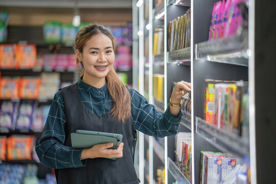 Good looking hardware store worker woman counts stock with a digital tablet. A young lady employee in uniform holds a touchpad face camera smiling.