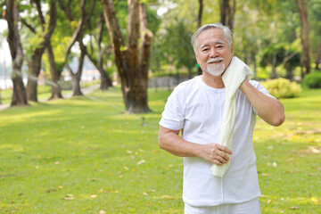 Tired heat and hot asian senior man practice yoga excercise, tai chi tranining and stretching while wipe the sweat away for healthy in park outdoor.  Happy elderly outdoor lifestyle concept