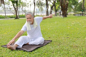 Asian senior man practice yoga exercise, stretching, tai chi tranining and meditation while sitting on yoga mat for healthy in park outdoor after retirement. Happy elderly outdoor lifestyle concept