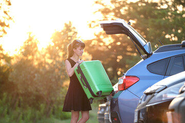 Young woman driver taking out suitcase bag out of her car. Travelling and vacations concept