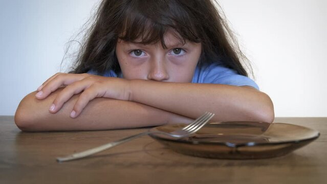Hunger during world food crisis. A sad child feel hungry by the empty plate on the table. A concept of meal crisis and financinal problems in the world.
