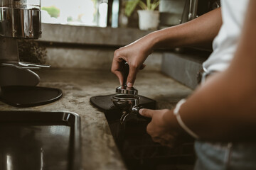 Barista using a tamper to press ground coffee into a portafilter. Coffee maker concept..
