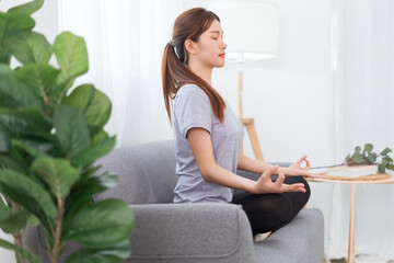 Obraz premium Yoga exercise concept, Young Asian woman doing yoga exercise in lotus pose on couch in living room
