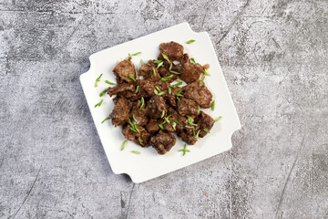 Pan fried chicken liver with herbs on a white square  plate on a dark background. Top view, flat lay