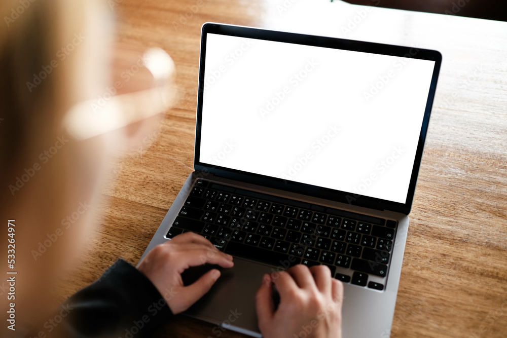 Wall mural Mockup image of a businesswoman using laptop with blank white desktop screen with coffee cup on wooden table in cafe.