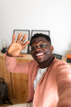 Black young man looking at camera waving hello during video call using phone. Man taking selfie. Copy space. Vertical.