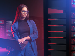 IT specialist woman. Girl with laptop in server room. Woman works as system administrator. Young businesswoman next to servers. IT business owner concept. IT company employee and server hardware