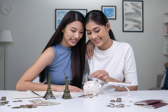 Young Asian lesbian couple plans to save money for a trip around the world. Travel budget concept, passport, monument model and aircraft toy in the picture. Lgbt couple lifestyle.