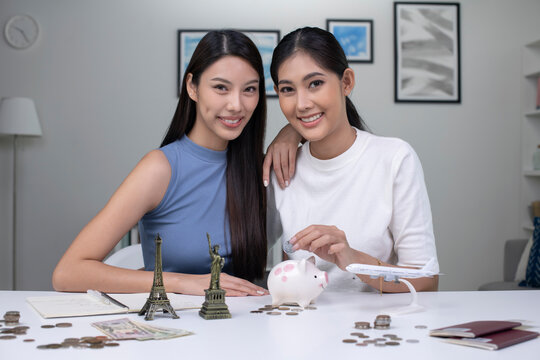 Portrait of Young Asian lesbian couple plans to save money for a trip around the world, looking at the camera.Travel budget concept, passport monument model and aircraft toy in the picture. 