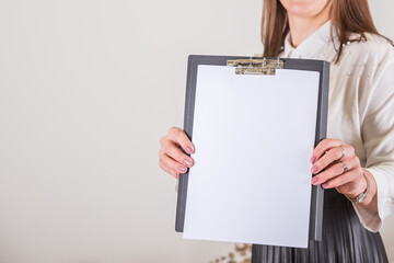 Naklejka premium Woman holding clipboard with a blank sheet of paper. Blank paper poster in female hands. Blank template for graphic designers portfolios. To do plans in business, blogging, educations