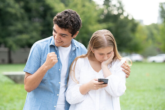 Teenager Girl Receiving Bad News On Phone And Hipocrite Boy Celebrating. Toxic Friendship Concept