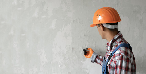 Builder in an orange helmet on a gray wall background pointing a finger at place for advertising,...