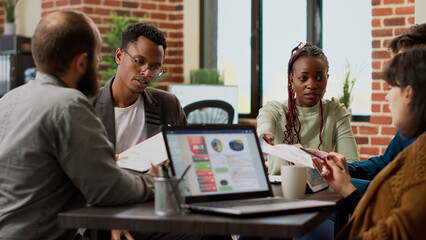 Diverse team of coworkers analyzing research information on documents and laptop display. People working on business report and presentation, doing teamwork partnership in office.