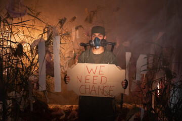 A man in a gas mask holding poster with words We Need Change. burning plastic trash on the...